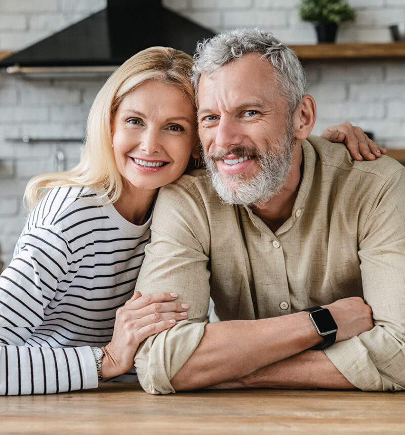 Portrait of middle aged couple hugging while standing together in kitchen at home